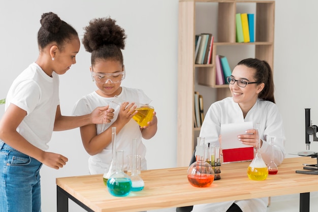 A middle school science teacher conducting a chemistry experiment with students. The teacher is demonstrating the experiment while the students observe attentively. The classroom is well-equipped with lab materials and safety equipment.