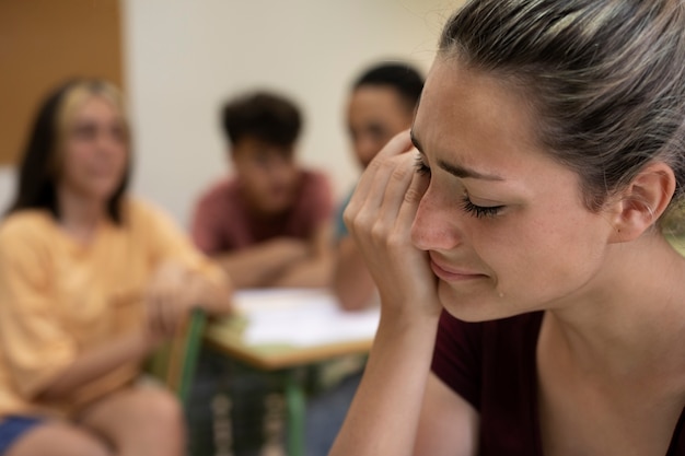A close-up shot of a student's hands clasped together in a classroom, conveying anxiety and uncertainty. The background is intentionally blurred, focusing on the emotional stress.