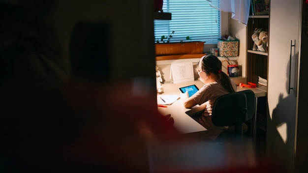 A student sitting alone in a dorm room, looking overwhelmed while studying. The room is dimly lit.