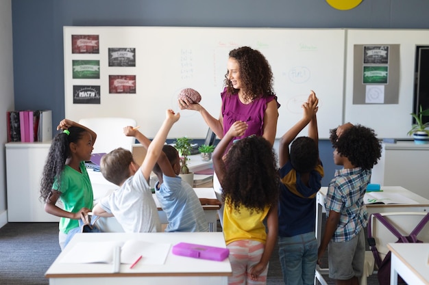 A teacher leading a classroom discussion in a diverse elementary school, with students raising their hands to participate.