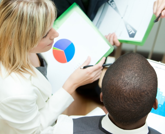 A diverse group of people discussing financial plans, each with personalized charts and graphs displayed on tablets. The setting is a modern co-working space with a focus on collaborative financial planning.