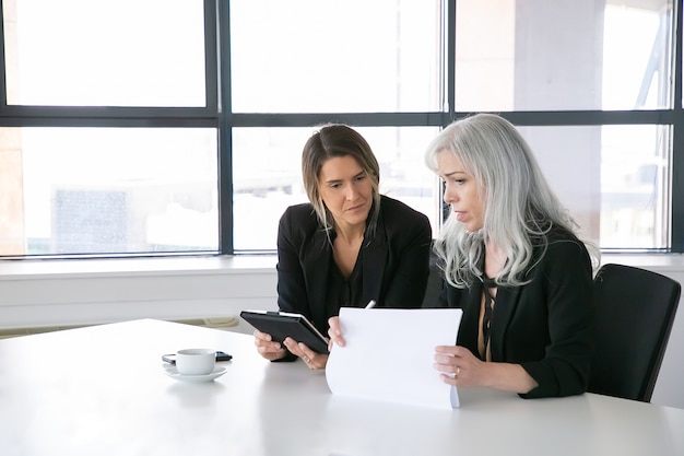 A professional financial advisor meeting with a client in a brightly lit office, reviewing documents related to insurance policies and risk management. The advisor is pointing to a specific section of the document, explaining its importance.