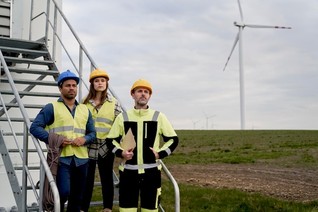 A diverse group of construction workers installing wind turbine blades on a wind farm in rural Iowa. The image captures the scale of the wind turbines and the activity of the work site, emphasizing the job creation aspect of renewable energy projects.