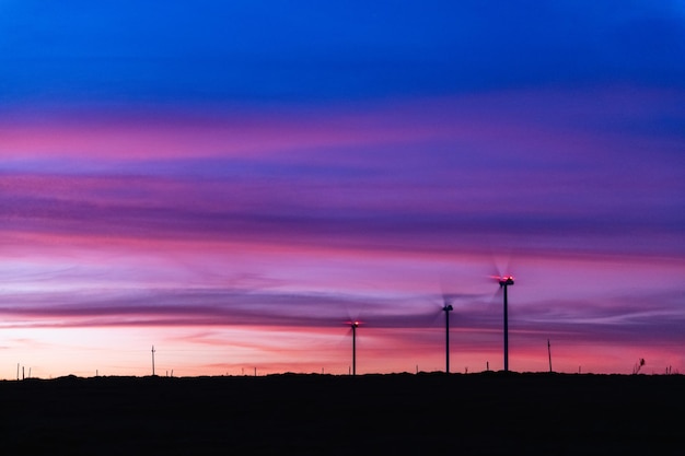 Wide shot of a modern wind farm at sunset, with large turbines silhouetted against the colorful sky, showcasing innovation.