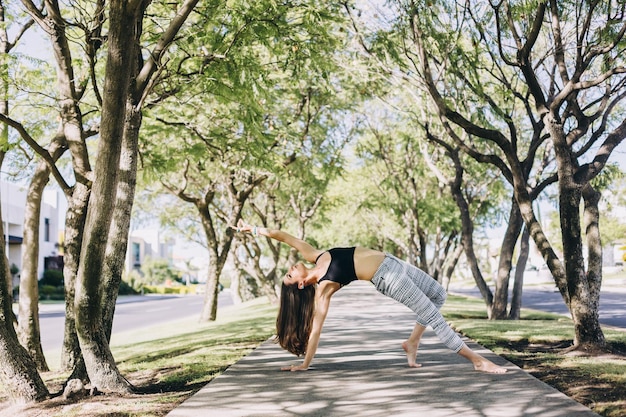 A person doing a yoga pose in a park. The background is a city park with people walking around.