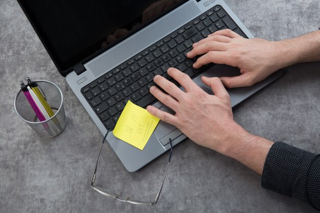 A close-up of a person's hands typing on a laptop, focusing on the resume writing process. There are sticky notes with keywords and phrases around the laptop.
