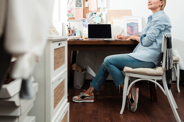 An individual working comfortably from their home office, with a laptop and ergonomic chair. The room is well-lit and organized, creating a productive workspace.