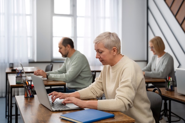 A senior professional attending a digital marketing workshop, actively participating with a laptop and taking notes. The setting is a modern training room with other professionals.